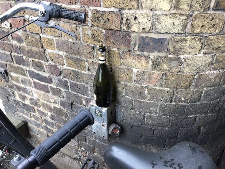 Brick wall, part of a black bicycle in the foreground, open green wine bottle on a small brick ledge